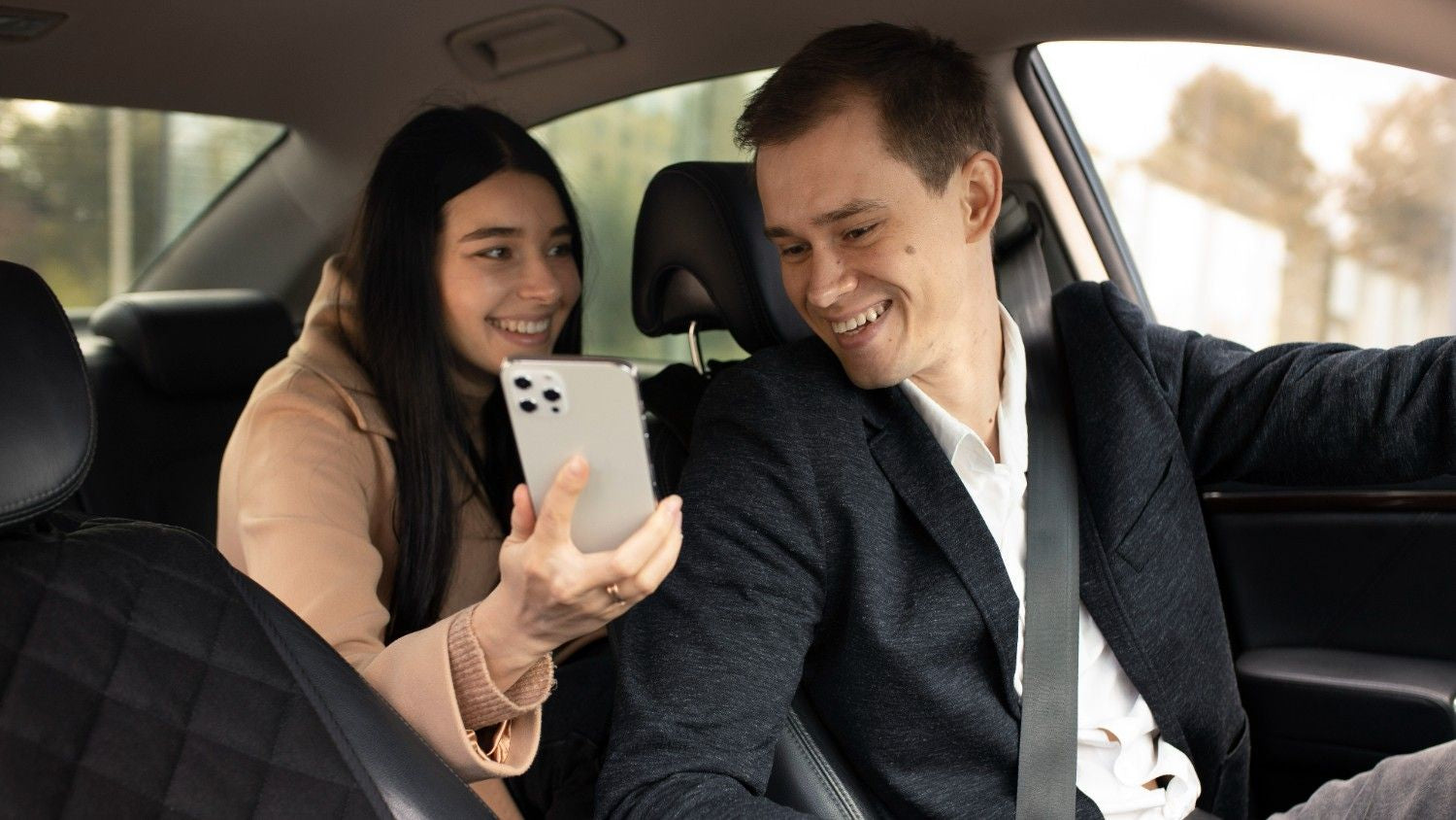 A woman in the back seat of a car showing her phone to a smiling taxi driver, illustrating how drivers can earn 20% commission on every eSIM sold through the Taxi eSIM Affiliate Program.