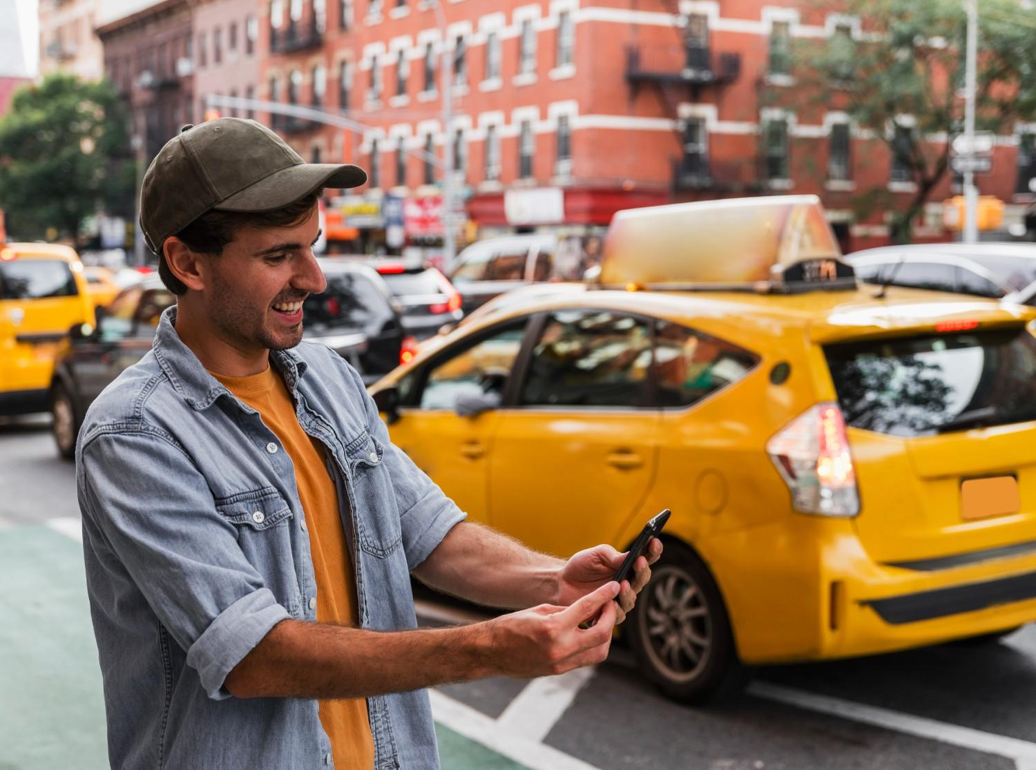
A smiling man in a city setting looking at his smartphone, with a yellow taxi in the background, illustrating signing up for a free account for the Taxi eSIM Affiliate Program.